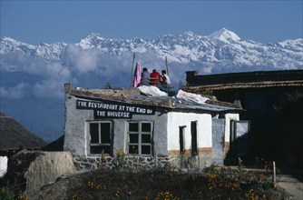 20027664 NEPAL  Himalayas The Restaurant At The End Of The Universe with three men sitting on the roof surrounded by snow capped mountain peaks