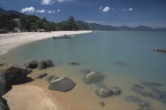 MALAYSIA, Penang, Batu Ferringhi, View along shore of quiet sandy beach with moored boat in middle
