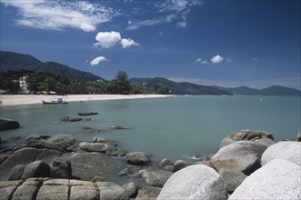 MALAYSIA, Penang, Batu Ferringhi, View over rocks and bay of turquoise water towards distant moored
