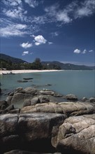 MALAYSIA, Penang, Batu Ferringhi, View over rocks and bay of turquoise water towards distant moored