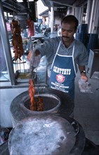 MALAYSIA, Penang, Georgetown, Man cooking tandoori chicken in circular clay oven at roadside stall