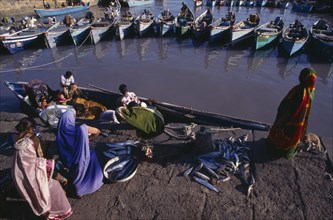 10128571 INDIA Gujarat Veraval Fishing harbour.  Women wait at harbourside while fishing boat unloads