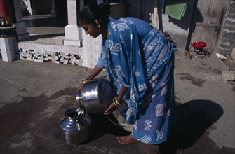 INDIA, Gujurat, Diu , "Young woman wearing blue, printed sari fetching water from well in street."