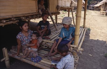 THAILAND, North, Mae Sai , Karen refugee mother feeding child with four other children sitting in
