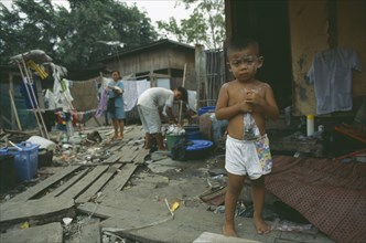 THAILAND, Bangkok, Klong Toey. Child standing by women hanging washing in slum housing area