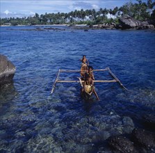 INDONESIA, Irian Jaya, Sorong, "Children in outrigger canoe on clear dark blue sea, rocks,palms "