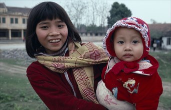 10137264 VIETNAM People Children Portrait of girl holding baby dressed  in red jacket and bonnet