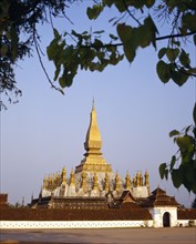 LAOS, Vientiane, Pha That Luang Sacred Stupa with gold spires and white walls part framed by tree