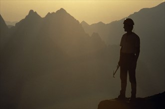 10001972 SPORT Mountineering Climbing Climber in safety helmet standing in partial silhouette against mountain peaks in early morning light. France  Chamonix  Alps.