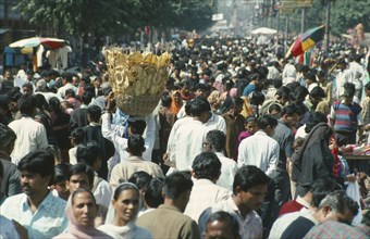 INDIA, General, Crowded street scene with man in centre carrying basket of bread on his head.
