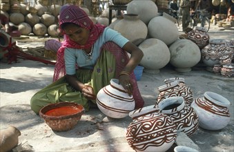INDIA, Rajasthan, Jodphur, Local woman in sari decorating pots by hand with red paint.