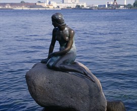 DENMARK, Zealand, Copenhagen, The Little Mermaid bronze statue sitting on a rock in calm water
