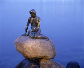 DENMARK, Zealand, Copenhagen, The Little Mermaid bronze statue seated on a rock at dusk with calm