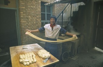 CHINA, Gansu Province, Lanzhou, "Smiling young man making noodles, holding long ribbons of dough in