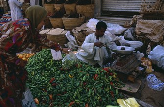 EGYPT, Upper Egypt, Luxor, Woman buying green chilli peppers in a street market with the vendor