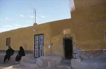 EGYPT, Upper Egypt, Aswan, Two Muslim women seated outside yellow coloured building.