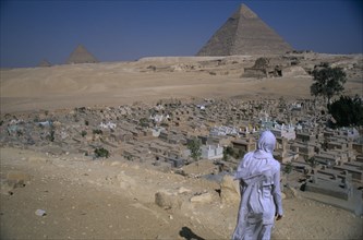 EGYPT, Cairo Area, Giza, The Pyramids with man standing in front of Muslim graveyard