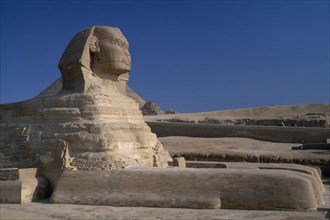 EGYPT, Cairo Area, Giza, The Sphinx restored with Pyramids and tourists on camels in the background