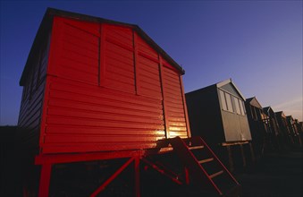 ENGLAND, Kent, Whitstable, Row of beach huts painted different colours on the beach in golden