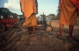 CAMBODIA, Kompong Thom, Building construction.  Cropped view of monks with hoe watching tractor and