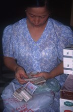 VIETNAM, Hanoi, Seated woman counting out bank notes.