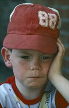 HEALTH, Emotional, Young boy wearing red hat with face resting on his hand in sulky mood.