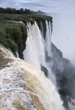 ARGENTINA, Misiones Province, Iguazu National Park, Iguazu Falls cascading over green cliffs.