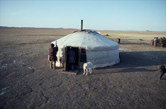 MONGOLIA, People, Ger or yurt in winter camp with dogs tied up outside and herdsman standing beside