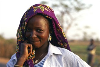 BURKINA FASO, Bobo Dioulassou, "Portrait of a smiling woman wearing a purple headscarf, working in