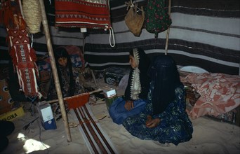 QATAR, People, Bedouin girls sitting inside tent decorated with hanging textiles weaving