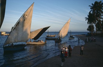 MOZAMBIQUE, Inhambane, Sailing boats and people on shore of sandy beach in soft golden light.