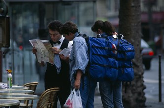 FRANCE, Ile de France, Paris, Tourists with backpacks asking waiter for directions.