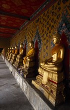 THAILAND, Bangkok Area, Bangkok, Wat Arun. Golden seated Buddha statues in cloister of Ordination