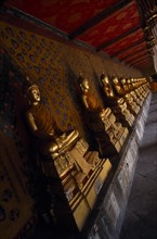 THAILAND, Bangkok Area, Bangkok, Wat Arun. Golden seated Buddha statues in cloister of Ordination