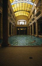 HUNGARY, Budapest, Gellert Baths.  Interior with bathers in swimming pool lined with carved pillars