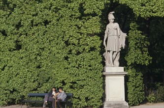 AUSTRIA, Vienna, Schonbrunn Gardens.  Classical statue against hedge with two visitors sitting on