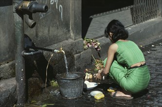MYANMAR, Yangon, Young woman using tap in street to wash dishes in the market.