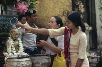 MYANMAR, People, Young women making offerings at Buddhist shrine with small seated Buddha figure