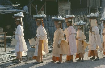 MYANMAR, Mandalay, Buddhist nuns wearing white and orange robes carrying trays of wrapped objects