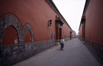CHINA, Beijing, The Forbidden City.  Cyclist on narrow street between red painted walls.