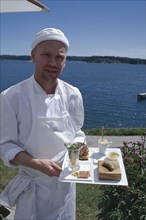 SWEDEN, Oaxen Island, Magnus Ech owner and chef holding a tray of food at Oaxen Skargards Krog