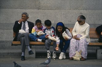 ENGLAND, London, Trafalgar Square, Asian family sitting together on a bench eating with girl
