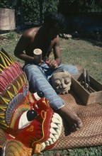 SRI LANKA, Kalutara, Man carving wooden masks next to a brightly painted example of his work