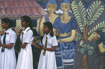 SRI LANKA, Colombo, Group of school girls dressed in white standing next to mural