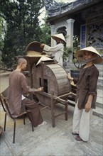VIETNAM, Hue, Monks husking rice in a traditional hand driven machine