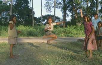 CAMBODIA, Angkor, Young girls with skipping rope playing beside road.
