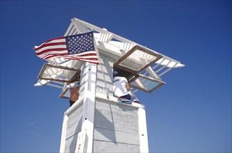 USA, Florida, Fort Lauderdale, Life Guard sitting on watch tower flying the stars and stripes flag