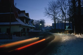 POLAND, Zakopane, Chocholow, Streaked red car lights in motion blur on road through snowy village