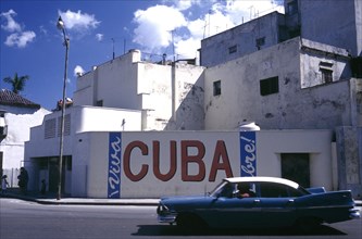 CUBA, Havana, Street scene with passing classic car and the words Viva Cuba painted on the wall