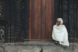 NEPAL, Bhaktapur, Man wrapped in white shawl sitting on the temple steps